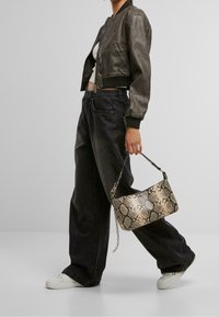 Sac à main à motif de serpent en beige et noir, doté d'une poignée courte et d'une touche de chaîne, associé à une veste bomber courte et un jean large.