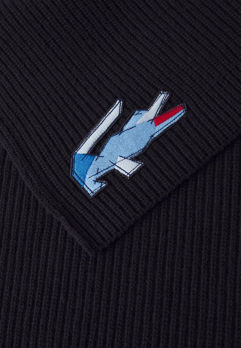 Czarna, prążkowana dzianina z haftowanym niebiesko-czerwonym wzorem logo. Logo ma kanciaste kształty i szczegółowe przeszycia.