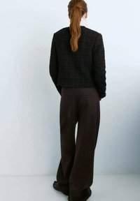 Czarna, teksturowana krótka kurtka o pudełkowym kształcie, w połączeniu z luźnymi brązowymi spodniami. Proste czarne buty dopełniają stylizację.