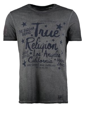 Mann trägt ein dunkelgraues True Religion Grafik-T-Shirt, dunkelblaue Jeans, schwarze Schuhe und einen schwarzen Schultertaschengurt quer über der Brust.