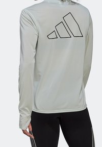 Ljusgrå långärmad träningsskjorta med en texturerad yta, med en svart Adidas-logotypdesign på baksidan.