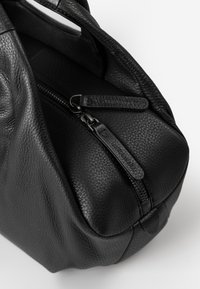 Zwarte leren handtas met een gestructureerde afwerking, ronde vorm, bovenhandvatten en dubbele ritssluiting. Kenmerkt subtiele logo-details op de ritstrekkers.