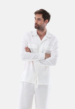 Weißes, strukturiertes Loungewear-Set mit einem Hemd mit Knöpfen und zwei vorderen Taschen sowie passenden Shorts. Leichter Stoff, lockere Passform.