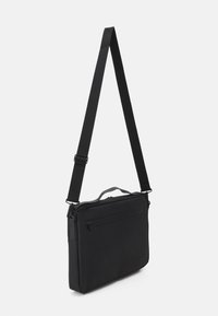 Borsa a tracolla nera con forma rettangolare, realizzata in materiale liscio. Include una tracolla regolabile e una tasca frontale con zip.