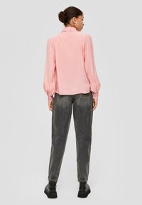 Hellrosa Bluse mit langen Ärmeln und Kragen, mit gefältelten Details und abgerundetem Saum, kombiniert mit hoch taillierten, dunkelgrauen Jeans und schwarzen Schuhen.