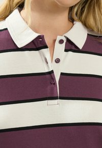 Lila und weiße gestreifte Polohemd mit schwarzen Streifen, ausgestattet mit einem Kragen und drei lila Knöpfen am Hals. Weiche Stofftextur.