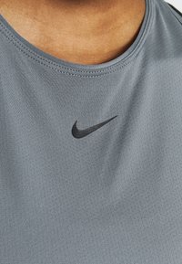 Szara koszulka sportowa wykonana z oddychającego materiału. Posiada okrągły dekolt i czarne logo Nike na lewej piersi.