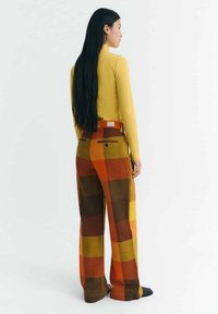 Yellow ribbed long-sleeve top paired with wide-leg pants featuring a checkered pattern in orange, brown, and yellow hues.