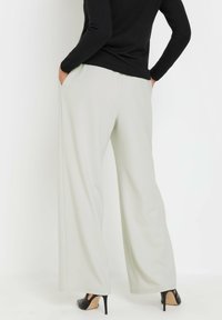 Hellegraue, weit geschnittene Hose aus weichem Stoff, mit Seitentaschen und elastischem Bund, kombiniert mit schwarzen High Heels.