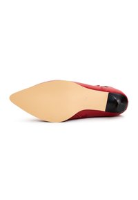 Chaussure à talon haut en cuir rouge avec un bout pointu et un accent noir lisse sur le talon. La semelle est en matériau beige légèrement texturé.