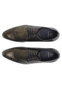 Black leather shoes with intricate gold leaf pattern, pointed toe, and six lace holes. Textured interior with branding visible.