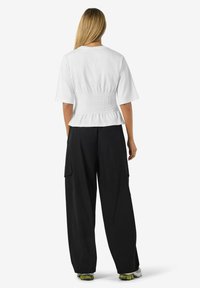 Balti trumpa rankovėmis bluzonė su surinkta juosmens detale, derinama su laisvomis juodomis krovinių kelnėmis, turinčiomis šonines kišenes.