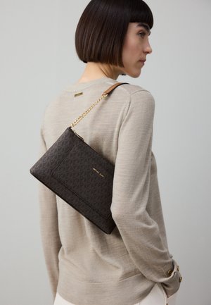 Barna mintás borítéktáska arany színű fém részekkel és láncos pánttal, bézs pulóver fölött a vállon viselve, texturált anyagból.