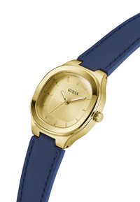 Ρολόι σε χρυσό τόνο με υφή στο καντράν και οκταγωνική κάσα. Μπλε δερμάτινο λουράκι με αντίθετες ραφές και πλευρικό κουμπί για ρυθμίσεις.