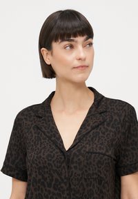 Kratka majica s crnim leopard uzorkom, kratkim rukavima, V-izrezom, detaljem džepa i kontrastnim rubovima. Izrađena od glatkog materijala s mekanom teksturom.