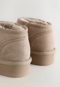 Tanowe zamszowe botki za kostkę z miękkim futerkiem z materiału syntetycznego, okrągłym noskiem, wzmocnionymi szwami i płaską gumową podeszwą.