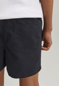 Pantalones cortos de color azul marino oscuro, confeccionados en tela de algodón, con un bolsillo trasero con una solapa triangular y un dobladillo cosido para mayor durabilidad.