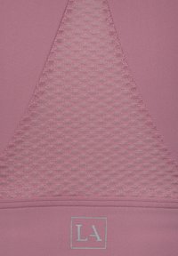 Light pink athletic top with a textured mesh triangular panel and a smooth lower section, featuring a subtle "LA" logo in blue.