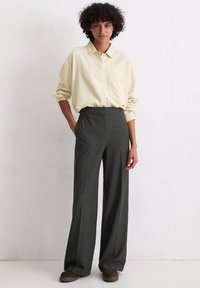 Lichtgele oversized shirt met een kraag, gecombineerd met donkergrijze gestreepte wijde broek. Gladde stoftextuur, casual fit ontwerp.