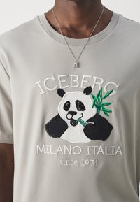 Szara bawełniana koszulka z haftowanym graficznym motywem pandy trzymającej bambus, z napisem "ICEBERG MILANO ITALIA od 1974" poniżej w białej nici.