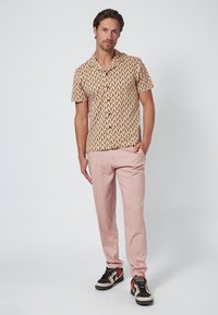 Camisa de manga corta en amarillo con un patrón en zigzag rojo y marrón, combinada con pantalones rosa claro y zapatillas negras-rojas-blancas.