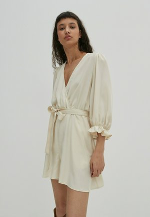 Crème wrap jurk met ballonmouwen, gefronste manchetten en een striktaille. Gemaakt van een soepele stof, met een diepe V-hals.