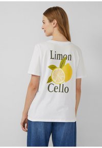 T-shirt en coton blanc à coupe décontractée, orné de graphiques de citrons verts et jaunes et du texte "Limon Cello" au dos, manches courtes.