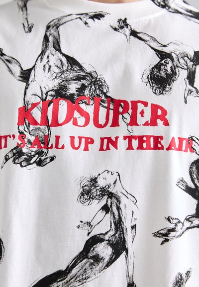 Balta medvilninė marškiniai su juodais dinamiškų figūrų brėžiniais, ant kurių drąsiai raudonai parašyta "KIDSUPER IT'S ALL UP IN THE AIR."