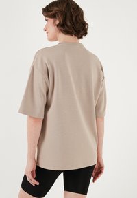 Beige kortærmet t-shirt med løs pasform, featuring en rund halsudskæring og glat tekstur. Sammen med sorte shorts.