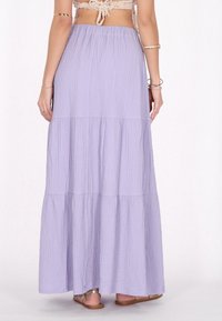 Lavendel, lagdelt maxi nederdel med struktureret stof. Elastisk talje og et luftigt design. Båret med flade sandaler, hvilket giver et afslappet udseende.