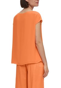 Blusa di seta arancione con maniche corte, vestibilità larga e scollatura arrotondata. Texture liscia e design minimalista, mostrata dal retro.