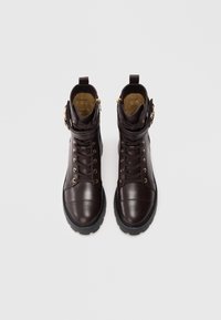 Bottines en cuir marron avec des garnitures dorées, des lacets et des fermetures éclair sur les côtés. Elles présentent une semelle en caoutchouc texturée et un col rembourré.