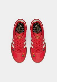 Κόκκινα αθλητικά παπούτσια με λευκές ρίγες, επάνω μέρος από σουέτ και δίχτυ, κεντήματα με λουλούδια και εσωτερική σόλα με σχέδιο. Επίπεδη σόλα από καουτσούκ.