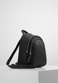 Černý koženkový batoh s dvěma zipovými přihrádky, nastavitelným popruhem, texturovaným povrchem a minimalistickým designem.