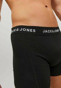 Male torso wearing black boxer briefs with "JACK & JONES" text on the waistband, shown against a plain background.