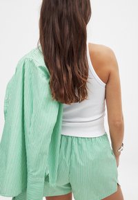 Zaļa un balta svītraina lielizmēra krekls, kas uzmests uz pleca; atbilstošas šortus ar elastīgu jostasvietu; pieguļošs balts topiņš.