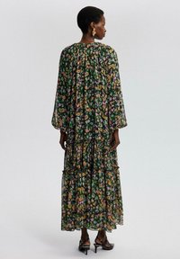 Lang, lagdelt kjole lavet af gennemsigtig stof med en mørkegrøn bund og flerfarvet blomstermotiv. Har lange ærmer og en rund halsudskæring.