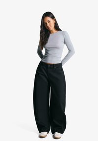 Graues, langärmliges enges Oberteil, kombiniert mit übergroßen schwarzen Jeanshosen, die eine hohe Taille und weite Beine haben, abgerundet mit weißen Sneakern.