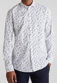 Chemise blanche à boutons avec un petit motif floral bleu marine, manches longues et col pointu. Tissu lisse avec une coupe classique.