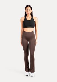 Schwarzer Sport-BH und braune, hoch taillierte Leggings aus glattem, dehnbarem Stoff. Das Modell steht vor einem schlichten weißen Hintergrund.