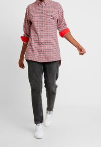 Camicia a quadri rossa e bianca con maniche arrotolate di colore rosso, abbinata a jeans grigio scuro e sneakers bianche.