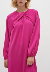 Fuksia mekko, jossa on pyöreä kaula-aukko, laskostettu etuosa ja pitkät puffihihat. Sileä kangas, jossa on joustava hihansuu.