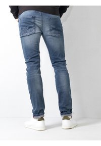 Jeans de mezclilla azul ajustados con un acabado desgastado, dos bolsillos traseros y dobladillos enrollados, combinados con zapatillas blancas con acentos verdes.