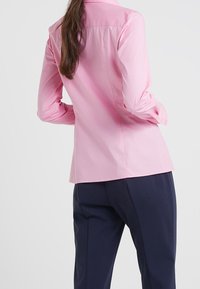 Camicia rosa chiaro a maniche lunghe con vestibilità sagomata, superficie leggermente texturizzata e polsini con bottoni, abbinate a pantaloni blu navy scuri.
