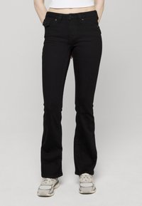 Zwarte denim flared jeans met een nauwsluitende taille, vijf zakken en een knoopsluiting aan de voorkant, gecombineerd met lichtgekleurde sneakers.