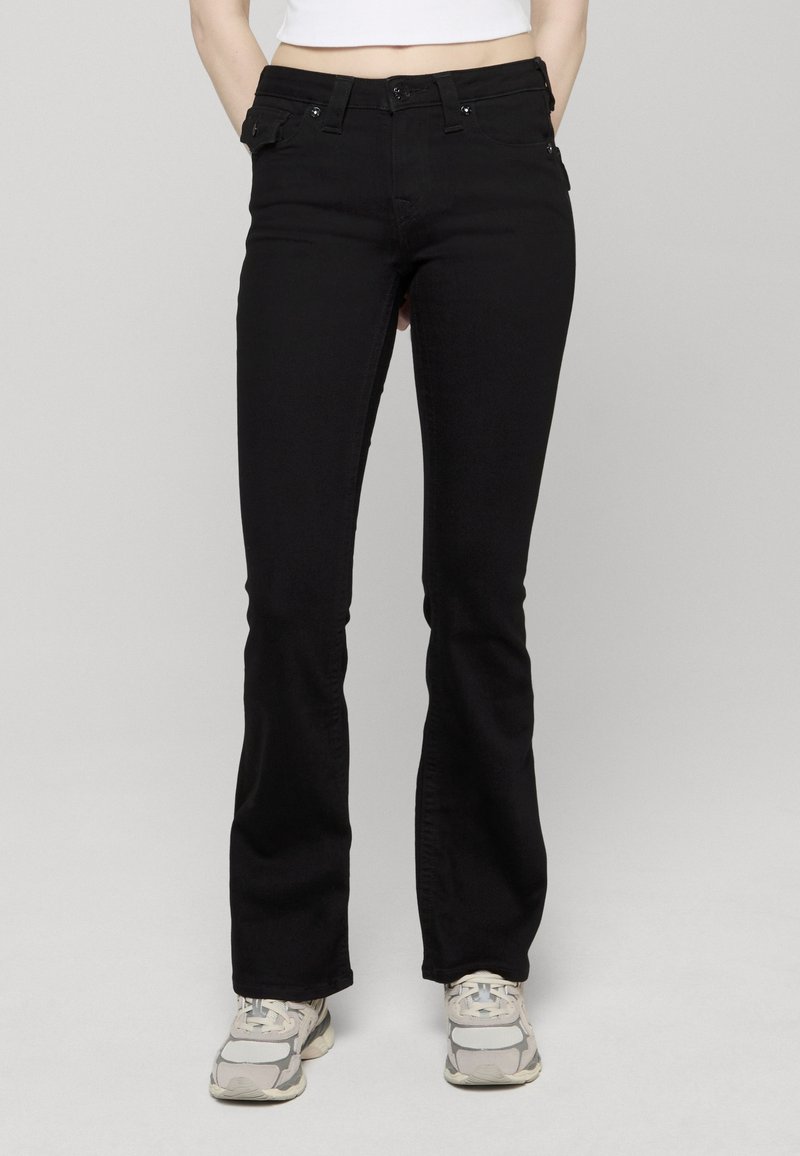 Zwarte denim flared jeans met een nauwsluitende taille, vijf zakken en een knoopsluiting aan de voorkant, gecombineerd met lichtgekleurde sneakers.