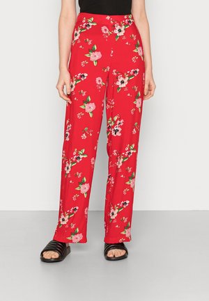 Red high-waisted wide-leg pants with pink and white floral patterns, worn with black slide sandals and a black sleeveless top.