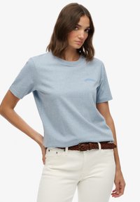 Lichtblauwe katoenen T-shirt met korte mouwen, voorzien van een subtiele tekstlogo in bijpassend blauw. Gemaakt in combinatie met witte jeans en een bruine gevlochten riem.