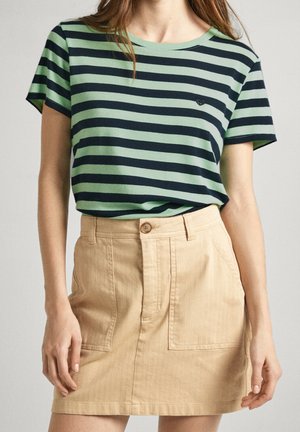 Vrouw draagt een groen-zwart horizontaal gestreept T-shirt, ingestopt in een beige rok met knopen en voorzakken.