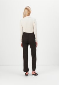 Ribbed, cream sweater paired with brown, pinstriped, wide-leg trousers. Plain, dark, flat sandals with ankle straps complete the outfit.